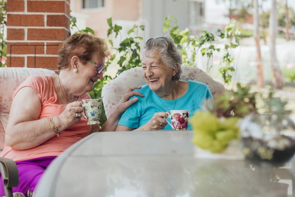 Two elderly women laughing over tea, reflecting healthy living and awareness through Body Mass Calculator in Australia