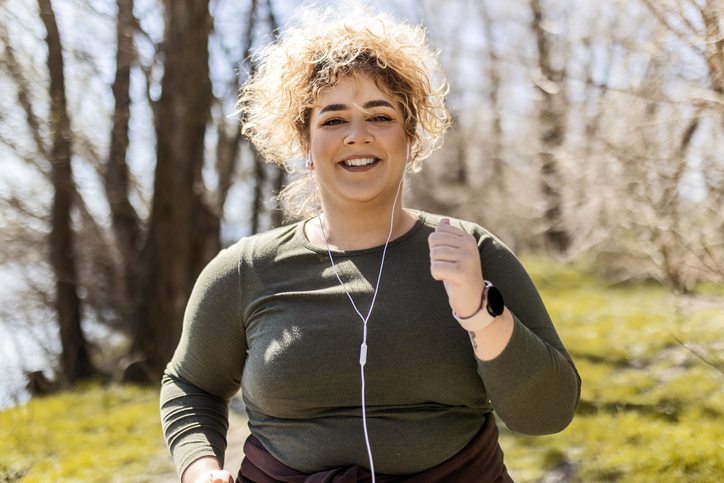 Young woman with curly hair running in the park, healthy lifestyle changes that weight loss surgery procedures support.