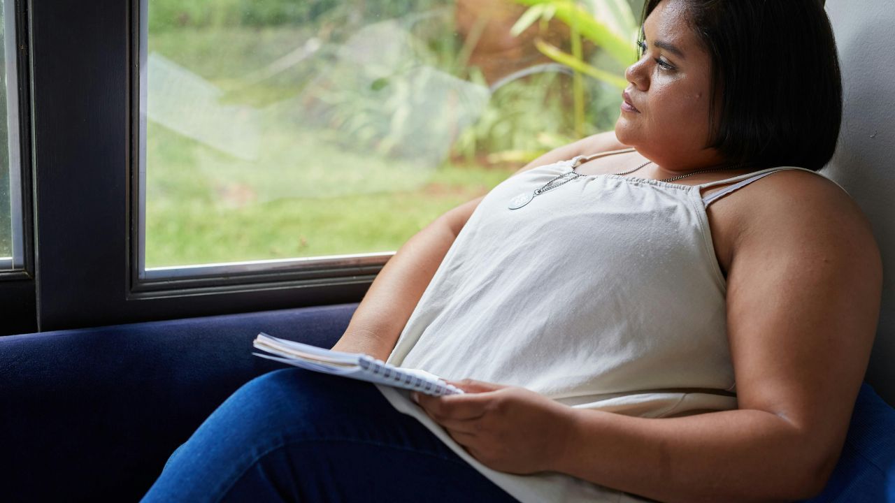 overweight woman sitting in chair with a book looking at the window