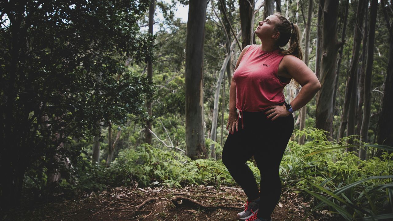 slightly overweight woman in athletic gear standing in a wooded forest